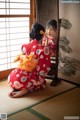 A woman in a red kimono sitting on the floor in front of a mirror.