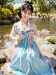 A woman in a blue and pink hanbok sitting on a rock.