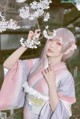 A woman in a pink and gray kimono holding a branch of a tree.