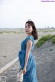 A woman in a blue dress standing on a beach.