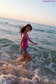 A woman in a pink tank top and denim shorts running into the ocean.