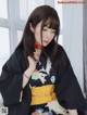 A woman in a black kimono sitting on a bed.