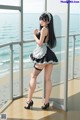 A woman in a maid outfit standing by a window.