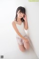 A woman in a white dress leaning against a wall.