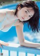 A woman in a blue bikini leaning on a railing by a pool.